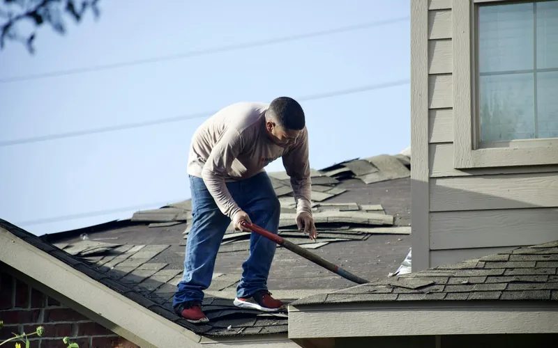 Worker removing damaged shingles from a residential roof